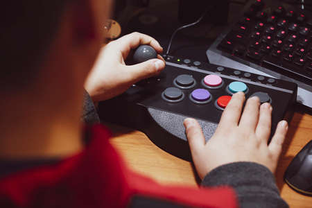 Imperia, Italy, 20/11/2019: Boy who presses the colored button of an arcade pad to play vintage video games, photo of a normal moment of life.の写真素材
