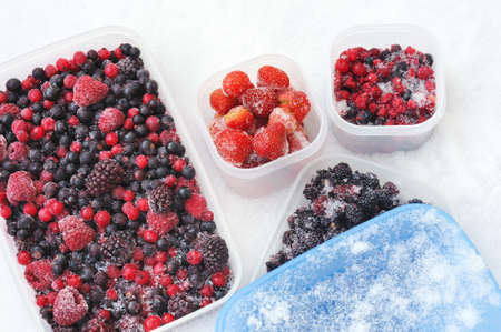 Plastic containers of frozen mixed berries in snow - red currant, cranberry, raspberry, blackberry, bilberry, blueberry, black currant, strawberryの写真素材