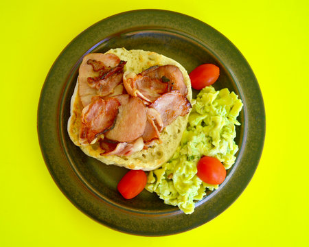 Healthy breakfast with bacon and avocado salad on a plate over yellow backgroundの写真素材
