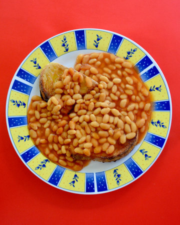 Baked beans with bread on a plate on a red background.の写真素材