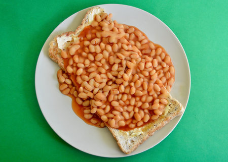 Baked beans in tomato sauce on toast bread on a green backgroundの写真素材