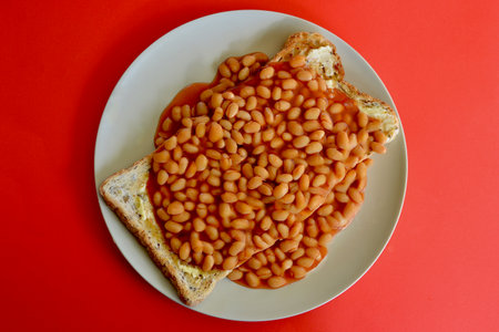 Baked beans in tomato sauce with toast bread on a red backgroundの写真素材