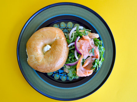 Bagel with salmon and arugula salad on a yellow backgroundの写真素材