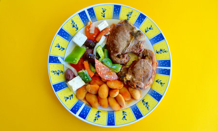Grilled lamb loin chops  with Greek salad in a plate on a yellow background.