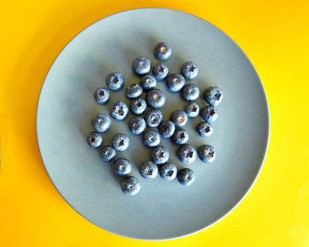 Blueberries in a plate on a yellow background. View from above.の写真素材