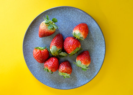 Strawberries on a gray plate on a yellow background, top viewの写真素材