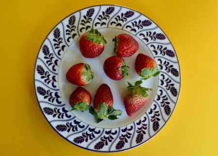 Strawberries on a plate on a yellow background. View from above.の写真素材