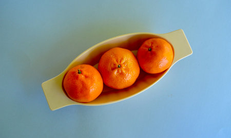 Mandarins in a yellow bowl on a blue background, top viewの写真素材