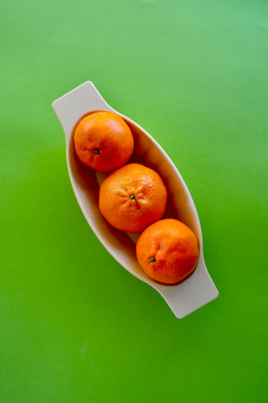 Mandarins in a white ceramic bowl on a green background.の写真素材
