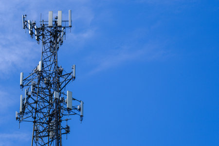 A photograph of the top portion of a cellular antenna tower against a blue sky with copy space