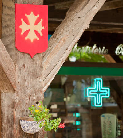 Ancient Cathar cross set against a pharmacy cross in a French village.の写真素材
