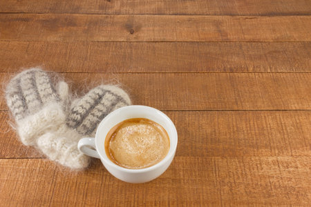 Woollen mittens with cup of fresh aromatic coffee on wooden background.