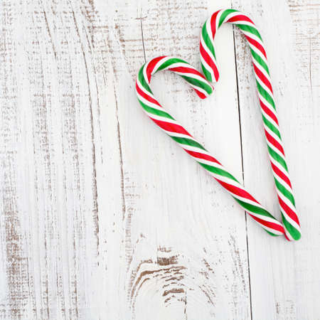Candy canes as heart on white wooden background.の写真素材