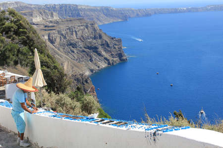 Seller with hat contrasting with the blue of the ocean in Santoriniの写真素材