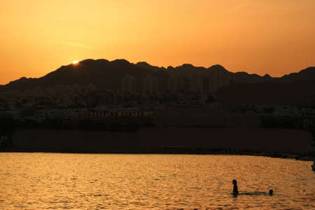 Kids bathing at Sunset in the Israeli town of Eilat with mountains of the Sinai peninsula in the background.の写真素材