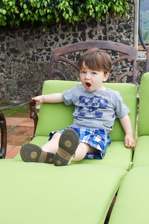 Boy sitting on a lounge chair and yawningの写真素材