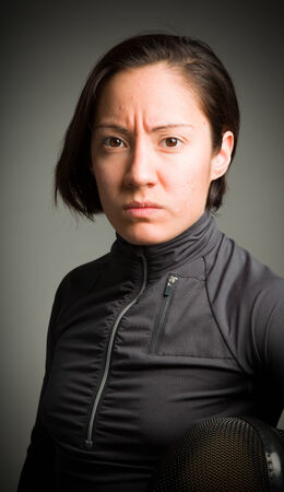 Portrait of a female fencer wearing fencing uniform and holding a mask isolated on gray backgroundの写真素材
