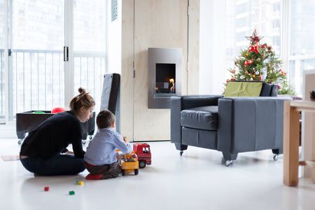 Mother and little son playing with toy trucks at home on Christmas Dayの写真素材