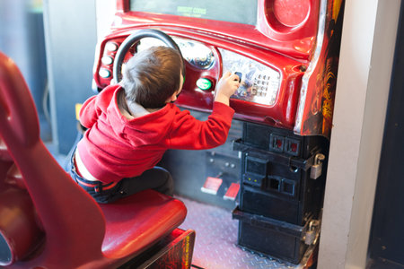 Rear view of a boy playing driving game at video game arcadeの写真素材