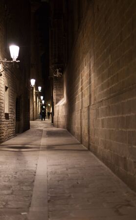 Empty narrow alley illuminated by street lamps at night, Barcelona, Catalonia, Spainの写真素材