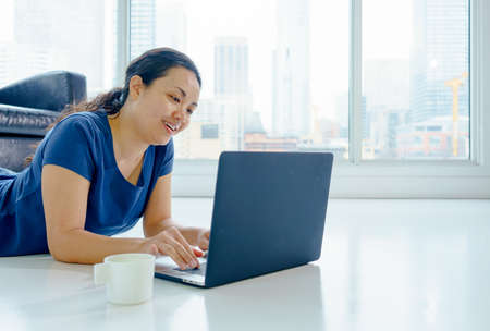 Woman indoors, laying on floor by window, day, using laptop. asian, long hair, adult
