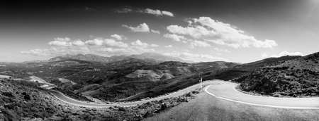 Winding road with field and mountain against cloudy sky, Crete, Greeceの写真素材
