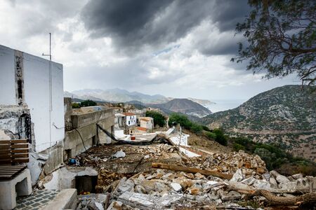 Old residential buildings with demolition debris and mountain against cloudy sky, Crete, Greeceの写真素材