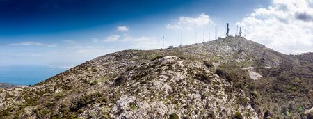 Communication tower on rocky mountain against sky by seaの写真素材