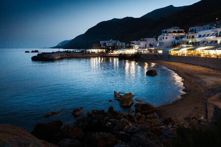 Beach by buildings against mountain at night, Crete, Greeceの写真素材