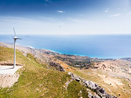 View of isolated wind turbine on rocky mountain overlooking blue seaの写真素材