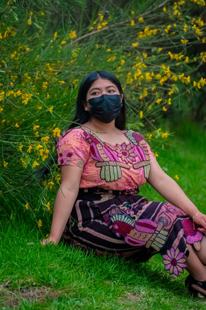 Asian woman wearing face mask and sit on the grass with yellow flowersの素材
