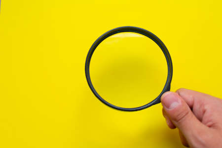 Hand holding a black magnifying glass isolated over a bright yellow background, on the right bottom cornerの写真素材