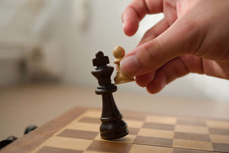 Hand holding a white pawn while it's hitting the black king in a check mate, chess game.の写真素材