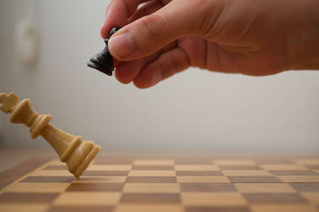 Hand holding a black pawn while it's hitting the white king in a check mate, chess game.の写真素材