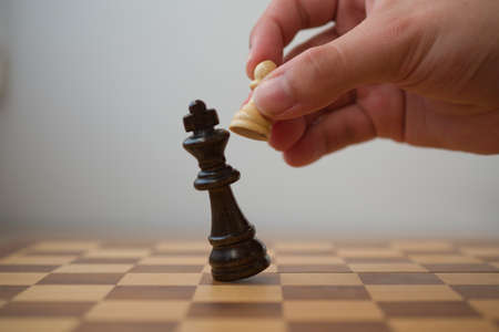 Hand holding a white pawn while it's hitting the black king in a check mate, chess game.の写真素材