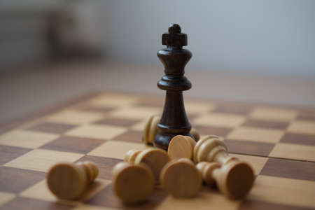 Black king chess piece is standing surrounded by defeated white pawns, victorious