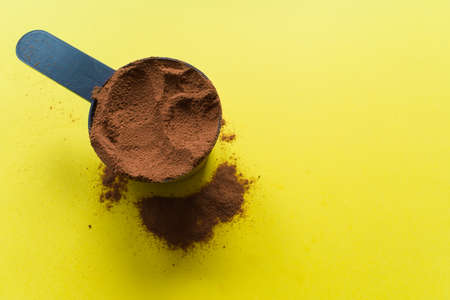Spoon with chocolate protein powder. Yellow background, top view.の写真素材