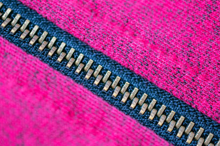 Close-up of a copper zipper crossing from top left to bottom right over a magenta and black fabric textureの写真素材