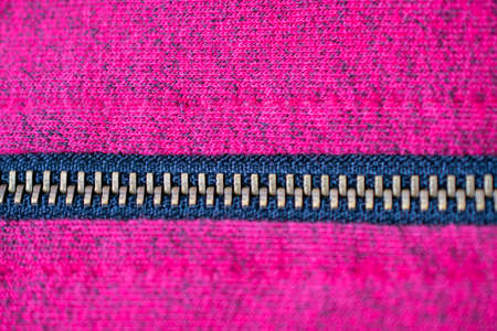 Close-up of a copper zipper crossing from left to right in the middle over a magenta and black fabric textureの写真素材