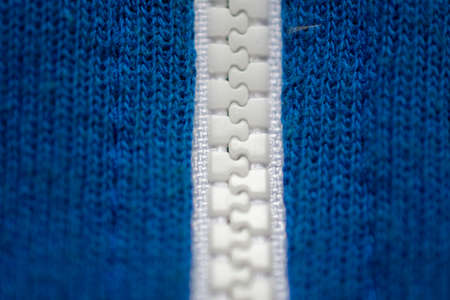 Close-up of a white plastic zipper closed in the middle of a blue fabric texture, from top to bottomの写真素材