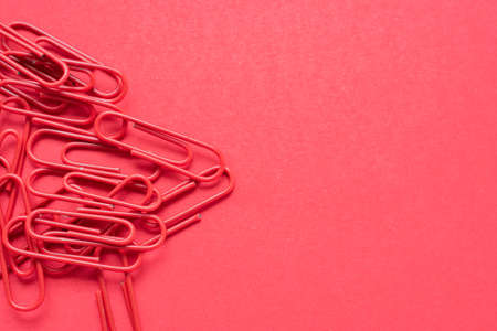 Bunch of red paper clips over a cherry red background on the left side, with copy spaceの写真素材