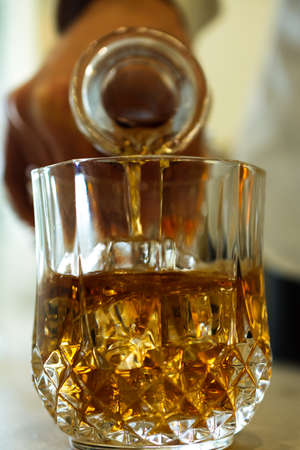 Close view of a bottle pouring whiskey on a glass with ice cubesの写真素材