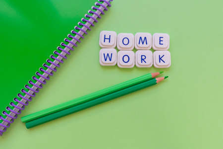 Home work message made with board game letters, with a green notebook and two green pencils, over a green background. Studies and work conceptの写真素材