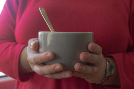 Hands of a woman with vitiligo, wearing a red jersey holding a bowl with a spoon in it. Breakfast...