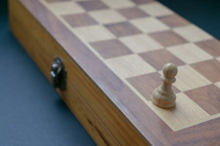 White chess pawn on the corner of a closed chess board, over a dark background. Isolation concept.の写真素材