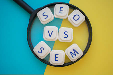 SEO vs SEM words over a magnifying glass, on a blue and yellow background. Search engines concepts...