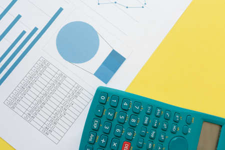 Scientific calculator and a paper with graphics and charts, over a yellow background. Business and economy conceptsの写真素材