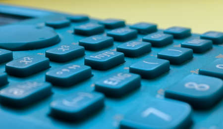 Close-up of a blue scientific calculator's buttons, over a blurred yellow background. Science and mathsの写真素材