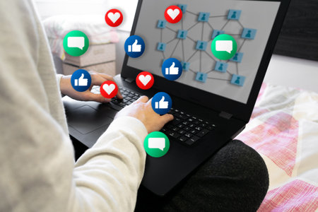 Young unrecognizable man in his bed, interacting on a social media with his computer.の写真素材