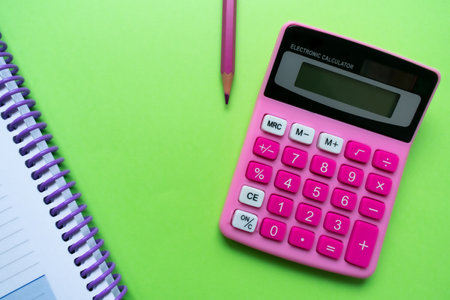 Pink calculator and pencil, and a corner of a notebook over a bright green background. Finances, maths conceptsの写真素材